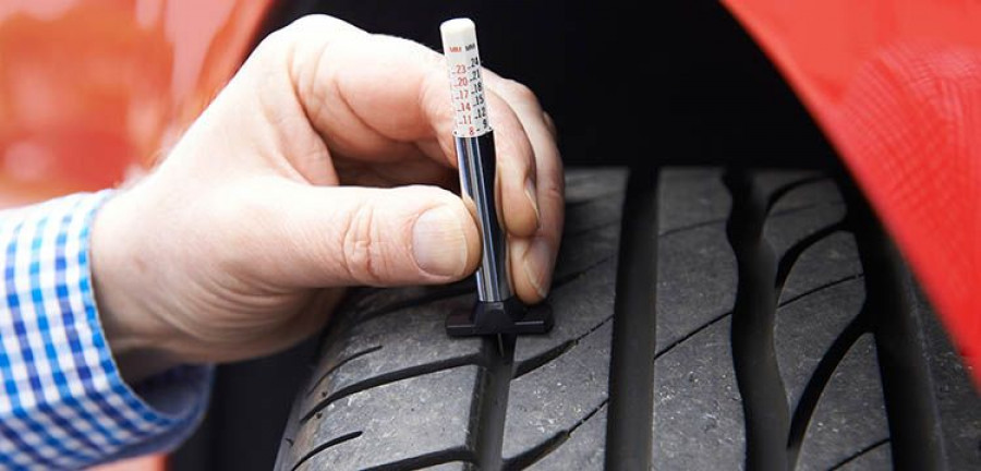 Close-up Of Man Checking Tread On Car Tyre With Gauge