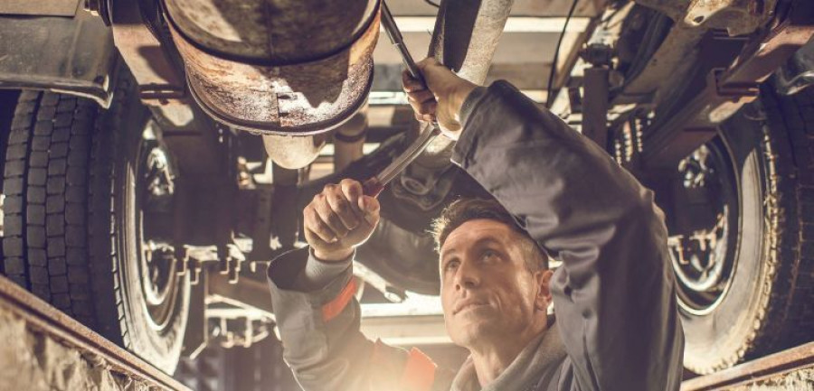 Male mechanic using socket wrench while working on chassis.